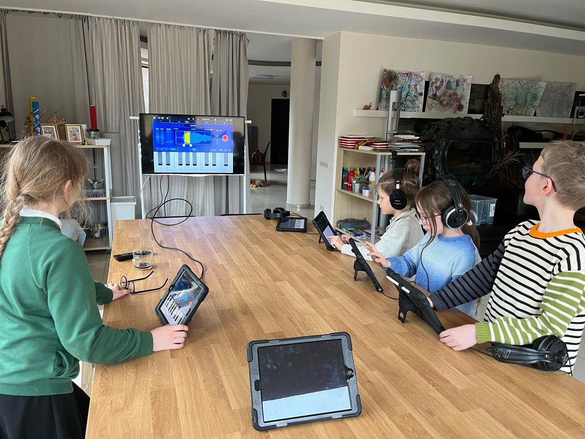 Vaikai studijoje su planšetėmis ir ausinėmis kuria muziką – technologijos kaip kūrybos kalba